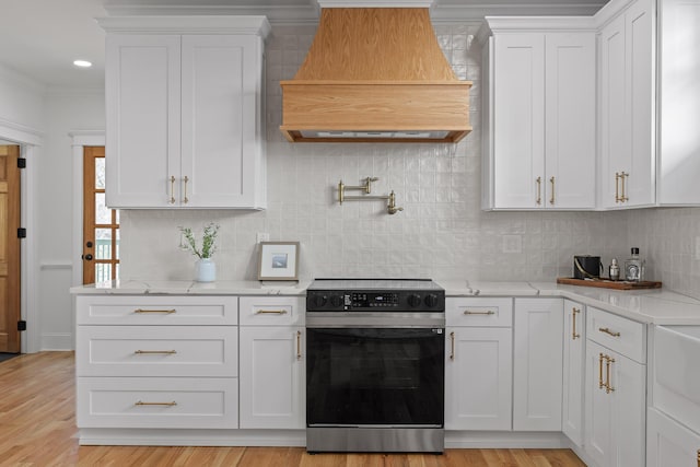 kitchen featuring light stone countertops, premium range hood, white cabinets, decorative backsplash, and electric range oven