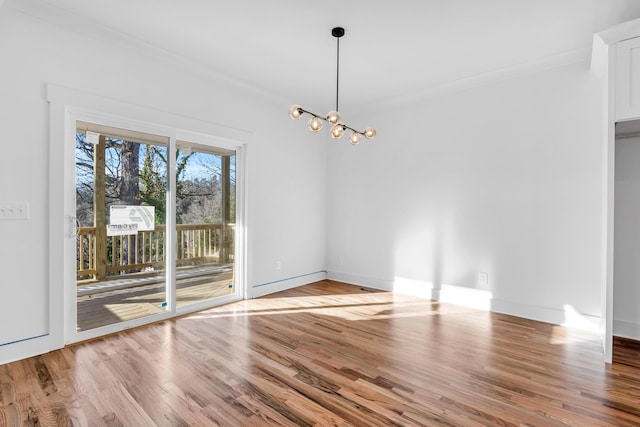 unfurnished dining area featuring crown molding, baseboards, wood finished floors, and an inviting chandelier