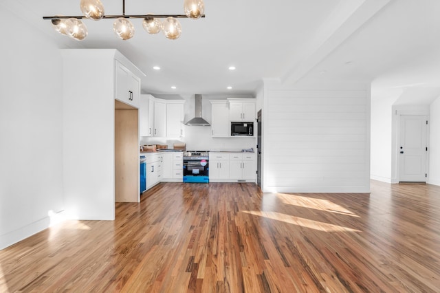 kitchen featuring black microwave, open floor plan, wall chimney range hood, light wood finished floors, and stainless steel range