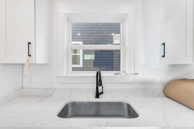 room details featuring light stone countertops, white cabinets, and a sink