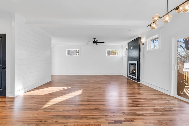 unfurnished living room with a large fireplace, wood walls, wood finished floors, and a ceiling fan