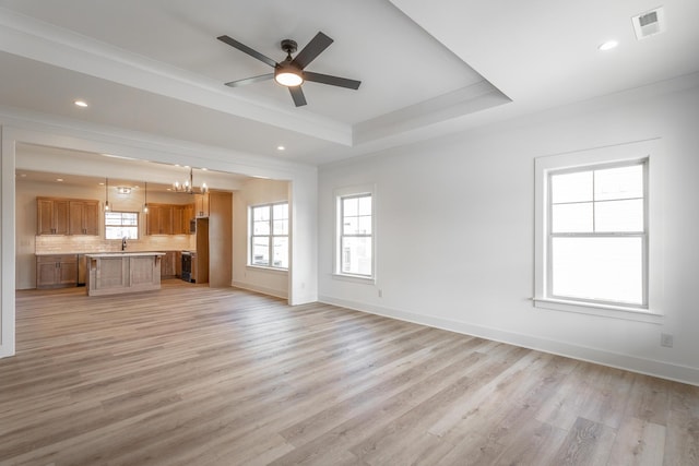 unfurnished living room with light wood finished floors, a tray ceiling, visible vents, and baseboards