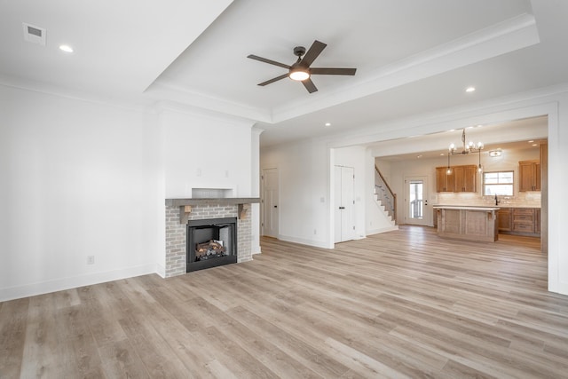 unfurnished living room with a fireplace, a raised ceiling, visible vents, ornamental molding, and light wood-style floors