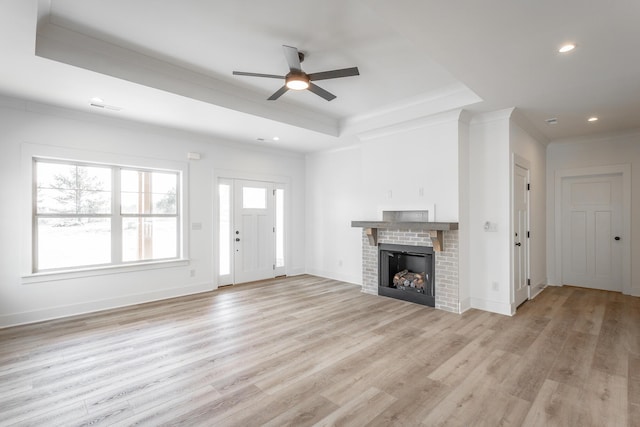 unfurnished living room with baseboards, a raised ceiling, crown molding, light wood-type flooring, and a fireplace