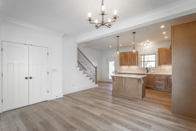 kitchen with light wood-style flooring, light countertops, ornamental molding, backsplash, and a center island