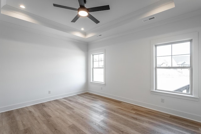 empty room with visible vents, a tray ceiling, light wood-style flooring, and baseboards