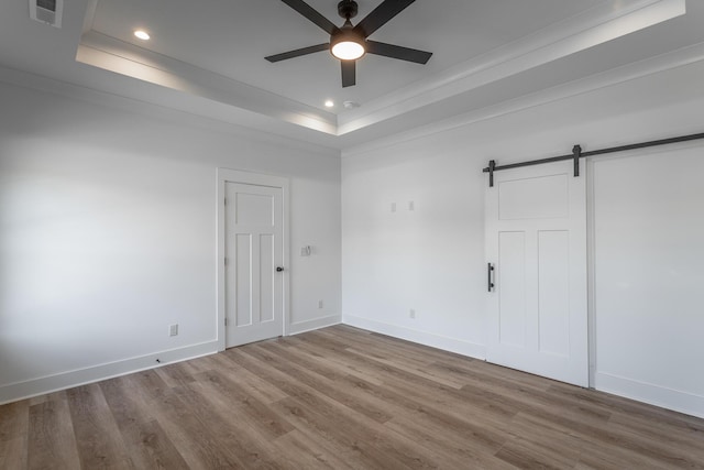 unfurnished room featuring a tray ceiling, a barn door, wood finished floors, and visible vents