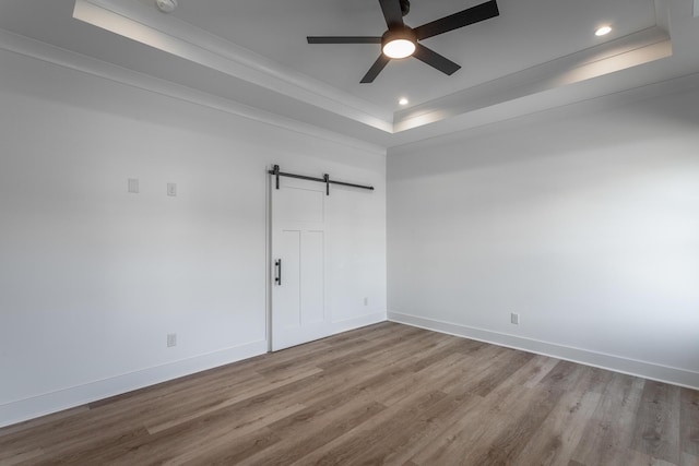 spare room with ceiling fan, a barn door, wood finished floors, baseboards, and a tray ceiling