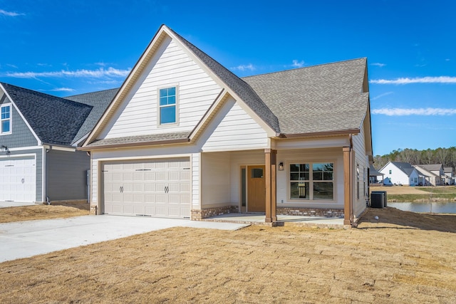 view of front of home with an attached garage, central air condition unit, a shingled roof, a water view, and concrete driveway