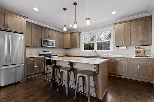 kitchen featuring dark wood-style flooring, a sink, appliances with stainless steel finishes, a center island, and crown molding