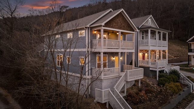 back of house at dusk with a balcony, a forest view, and stairs