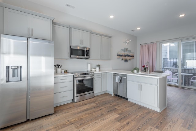 kitchen with visible vents, appliances with stainless steel finishes, wood finished floors, a peninsula, and a sink