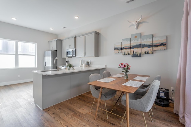 kitchen with a peninsula, wood finished floors, a sink, appliances with stainless steel finishes, and gray cabinets