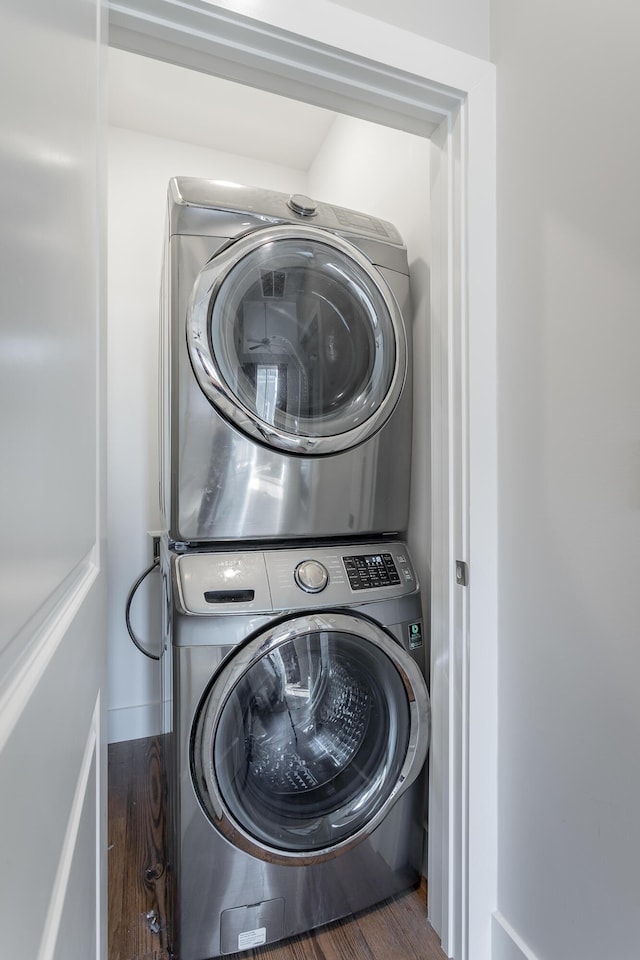 clothes washing area with stacked washer and dryer, wood finished floors, laundry area, and baseboards