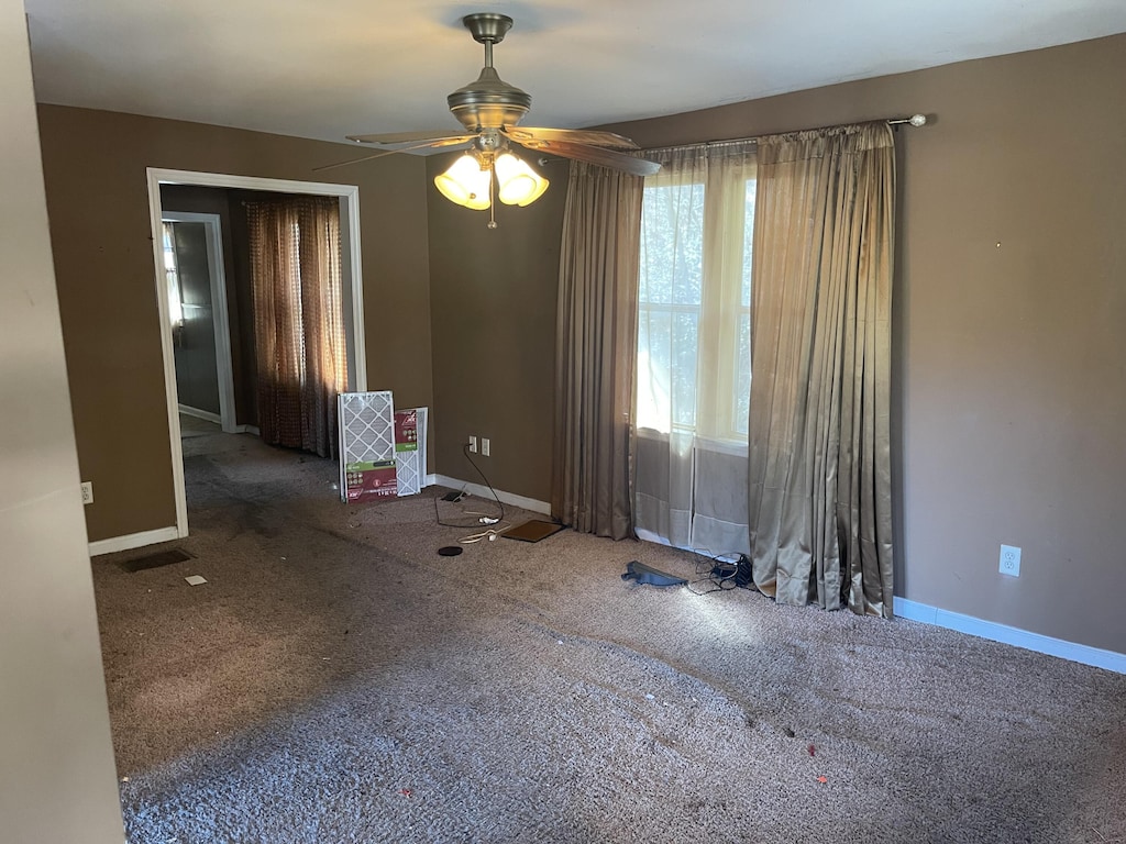 carpeted spare room with visible vents, a ceiling fan, and baseboards