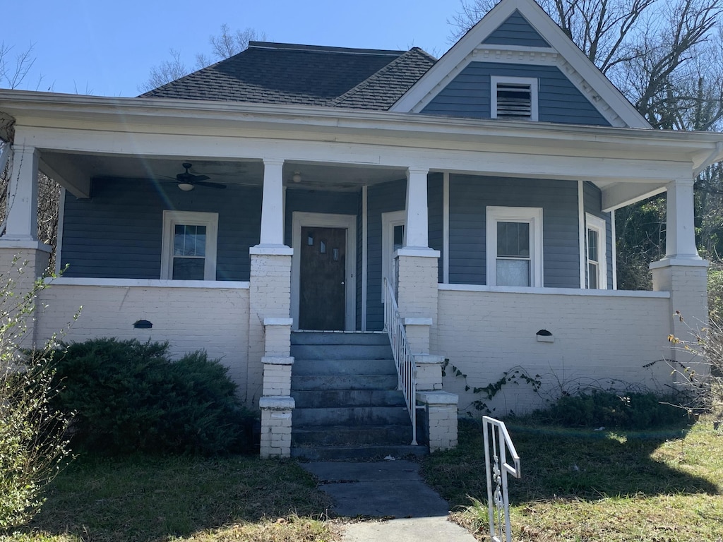 view of front facade featuring covered porch, roof with shingles, a ceiling fan, and brick siding