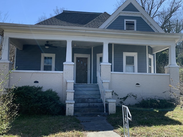 view of front facade featuring covered porch, roof with shingles, a ceiling fan, and brick siding