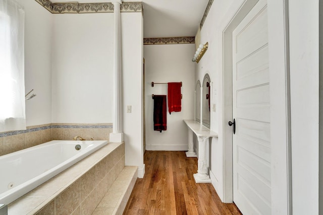 full bathroom with wood finished floors, a garden tub, and decorative columns