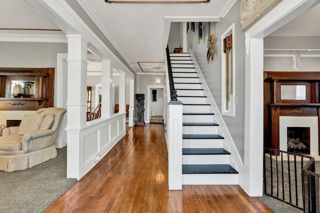 foyer entrance featuring ornate columns, a fireplace, stairs, dark wood-style floors, and crown molding