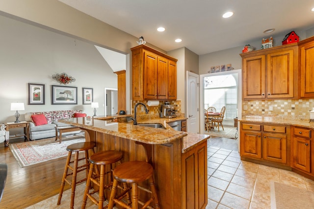 kitchen with light stone counters, a breakfast bar area, a sink, open floor plan, and tasteful backsplash