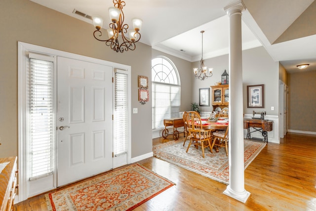 entrance foyer featuring light wood finished floors, decorative columns, visible vents, ornamental molding, and a chandelier