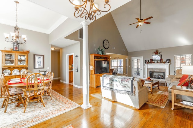 living room featuring high vaulted ceiling, light wood-style flooring, ceiling fan with notable chandelier, a fireplace, and decorative columns