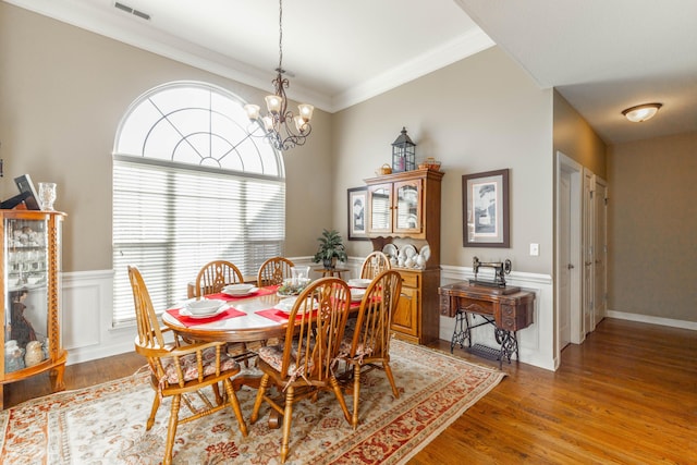 dining room featuring visible vents, a wainscoted wall, ornamental molding, light wood-type flooring, and a chandelier