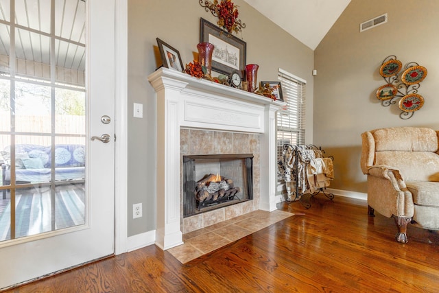 living area with baseboards, visible vents, a tiled fireplace, lofted ceiling, and wood finished floors