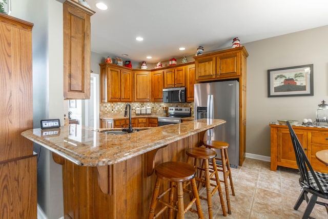 kitchen featuring stainless steel appliances, a sink, backsplash, light stone countertops, and brown cabinetry