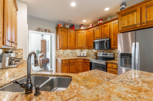 kitchen featuring light stone countertops, backsplash, stainless steel appliances, and a sink