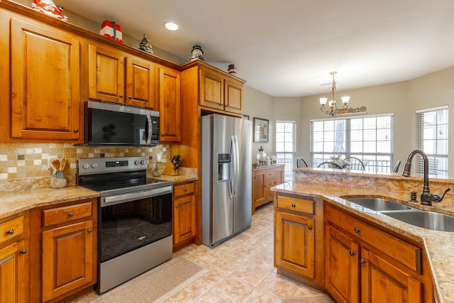 kitchen featuring brown cabinetry, a sink, stainless steel appliances, pendant lighting, and backsplash