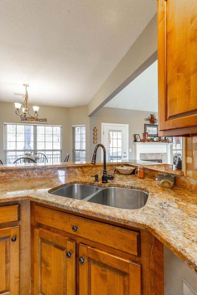 kitchen featuring a chandelier, a fireplace, a sink, light stone countertops, and brown cabinetry