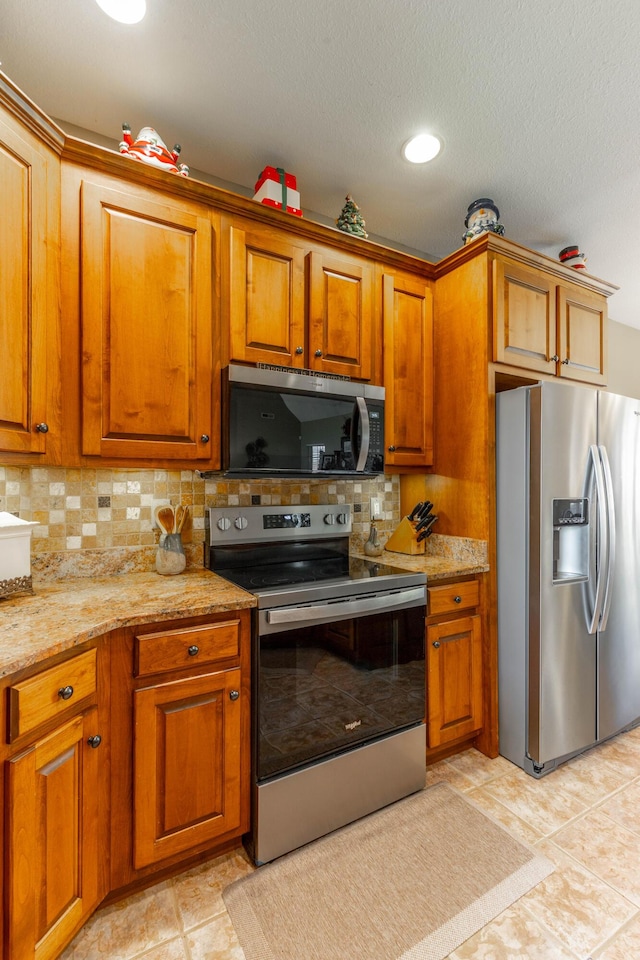 kitchen with light stone counters, appliances with stainless steel finishes, brown cabinetry, and decorative backsplash