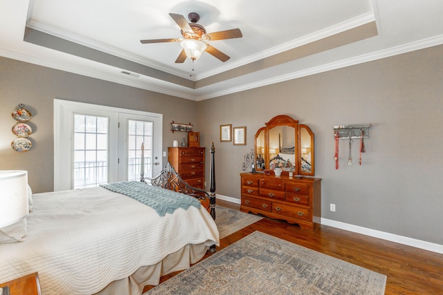 bedroom featuring a tray ceiling, visible vents, baseboards, and wood finished floors