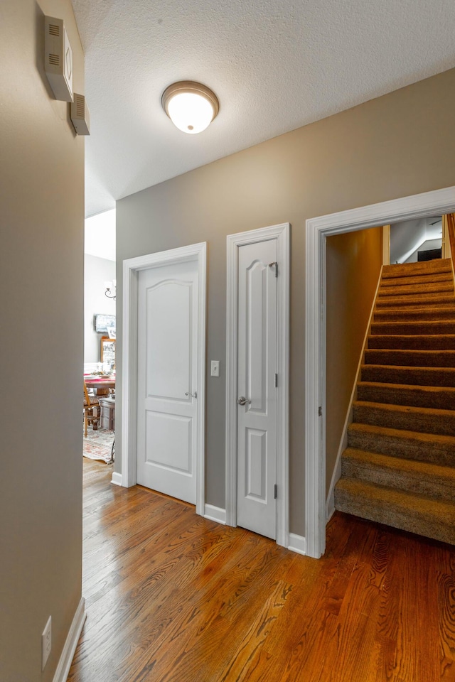 hall featuring stairs, a textured ceiling, baseboards, and wood finished floors