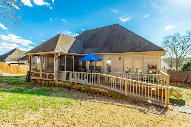 rear view of house with a deck, a yard, roof with shingles, and fence