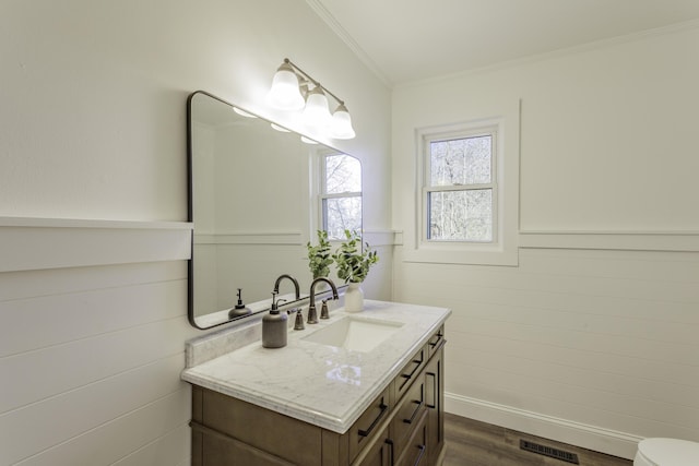 half bathroom featuring wood finished floors, vanity, visible vents, wainscoting, and crown molding