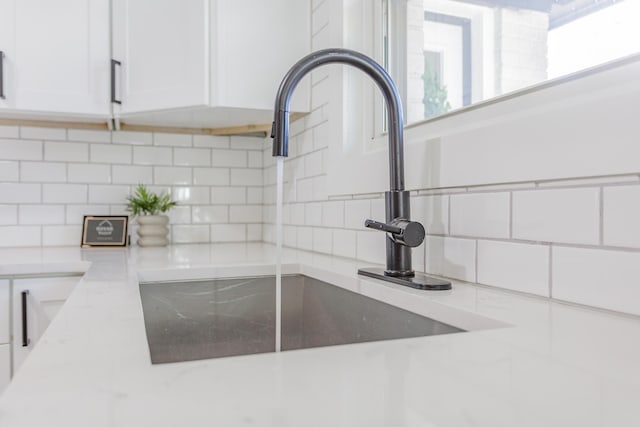 room details with decorative backsplash, a sink, light stone countertops, and white cabinets