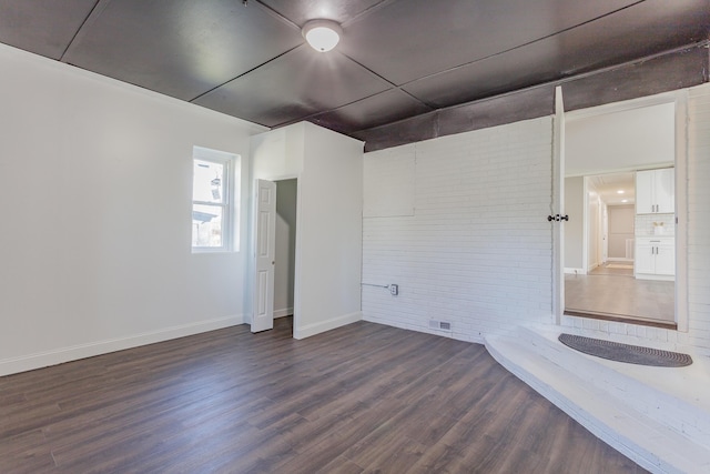 unfurnished room featuring dark wood-style flooring, baseboards, and brick wall