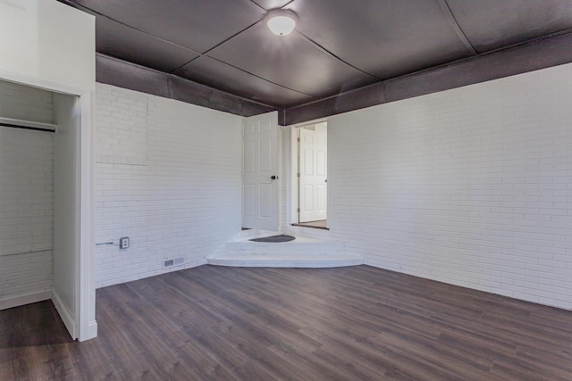 unfurnished room with brick wall, visible vents, and dark wood finished floors