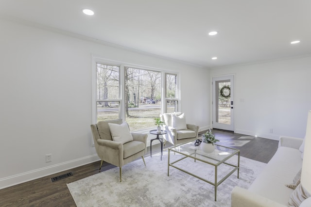 living area with baseboards, crown molding, visible vents, and wood finished floors