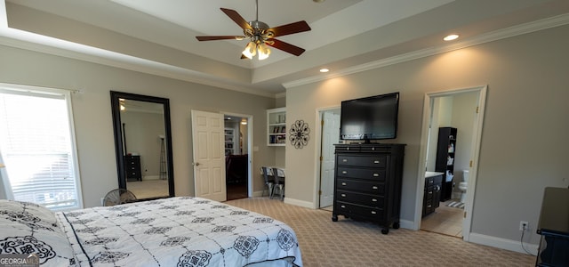 bedroom featuring light carpet, baseboards, a raised ceiling, ensuite bath, and ornamental molding