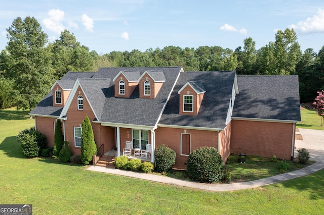 view of front of property with covered porch, a front lawn, a shingled roof, and brick siding