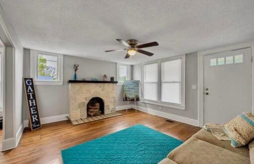 living room with baseboards, a ceiling fan, wood finished floors, a textured ceiling, and a fireplace