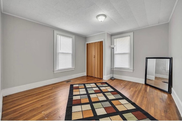 unfurnished bedroom featuring a textured ceiling, visible vents, baseboards, ornamental molding, and wood-type flooring