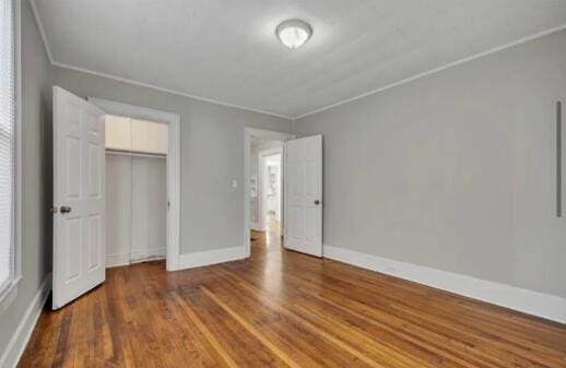 unfurnished bedroom featuring crown molding, a closet, wood finished floors, and baseboards