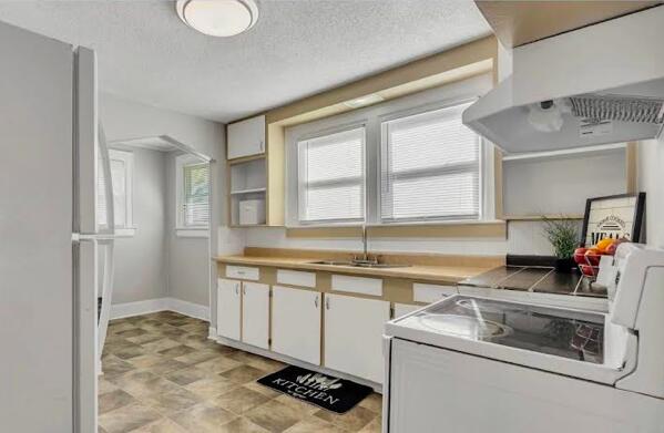 kitchen featuring freestanding refrigerator, a sink, a textured ceiling, plenty of natural light, and under cabinet range hood