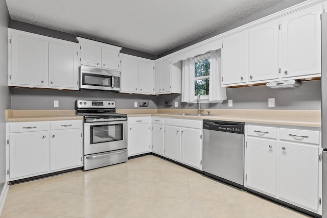 kitchen featuring stainless steel appliances, a textured ceiling, light countertops, white cabinetry, and a sink