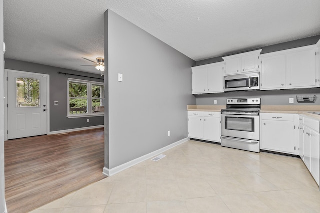 kitchen with a textured ceiling, baseboards, white cabinets, light countertops, and appliances with stainless steel finishes