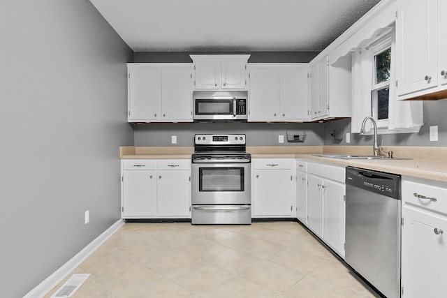 kitchen featuring baseboards, white cabinets, appliances with stainless steel finishes, light countertops, and a sink